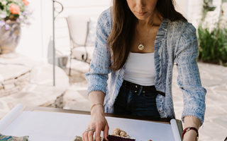 Founder Chelsea Secor is standing outside arranging fabric and wallpaper samples together for an interior design project